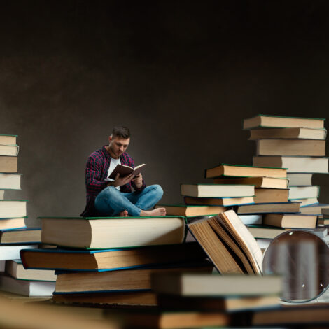 Little man reading among large books and textbooks Little man reading among large books and textbooks, scale effect. Gaining knowledge and education concept. Student studying the subject before the exam