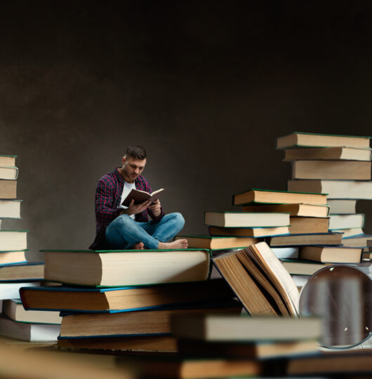 Little man reading among large books and textbooks Little man reading among large books and textbooks, scale effect. Gaining knowledge and education concept. Student studying the subject before the exam